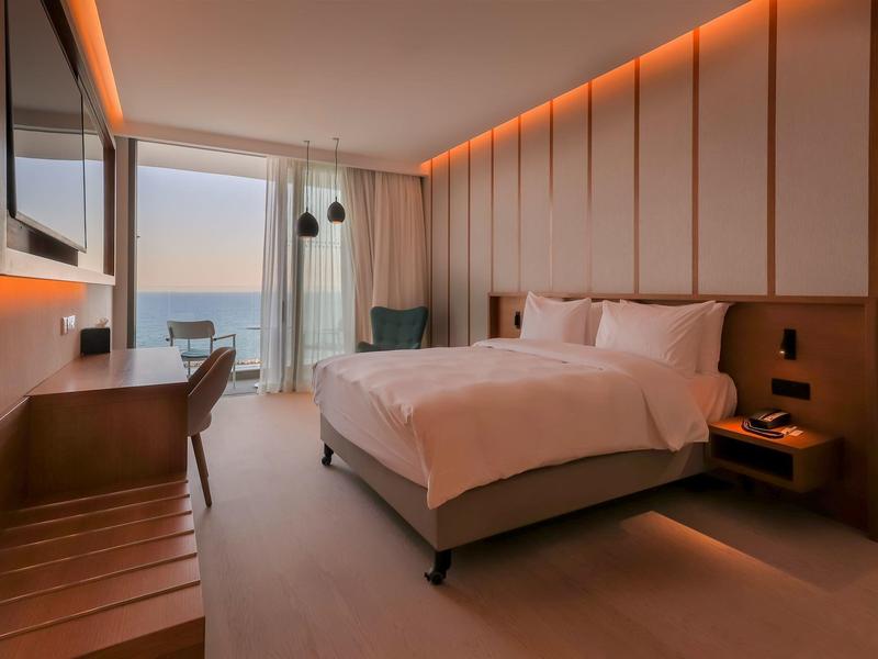 Modernes Hotelzimmer mit großem Bett, Schreibtisch, Meerblick und warmen LED-Beleuchtungselementen.