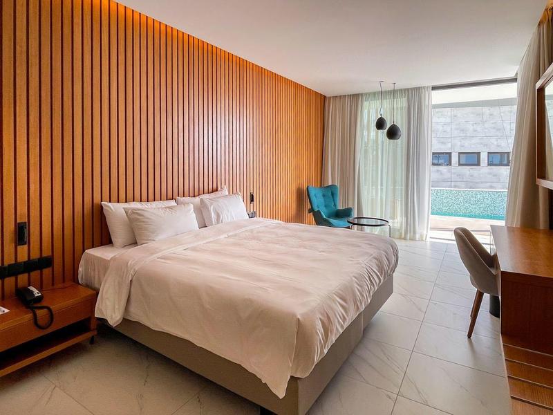 Moderndes Schlafzimmer mit Holzwand, großem Bett, Schreibtisch und Balkon mit Blick auf Pool.