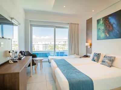 Modernes Hotelzimmer mit Doppelbett, Schreibtisch, Fernseher und Balkon mit Meerblick.