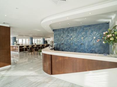 Moderní recepce se zakřiveným dřevěným pultem a modrou výzdobou na lesklé mramorové podlaze