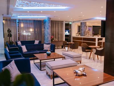 Moderně zařízená hotelová lounge s pohovkami, stoly a barem v pozadí.