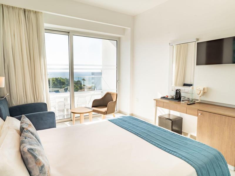 Modernes Hotelzimmer mit großem Bett, Schreibtisch und Meerblick vom Balkon