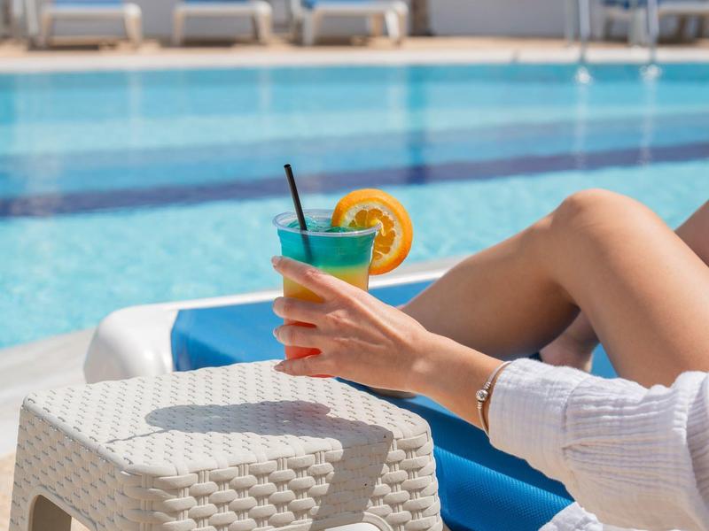 Person entspannt am Pool mit einem erfrischenden Getränk in der Hand.