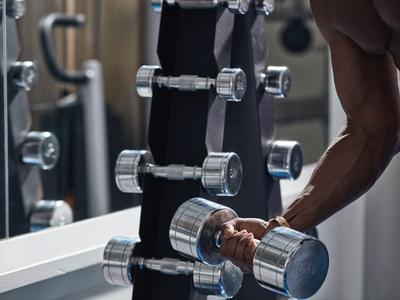 Osoba podnosząca hantle na siłowni przed lustrem