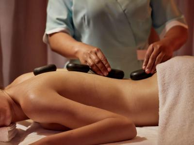 Person receiving a hot stone massage with warm stones on the back in a spa room.