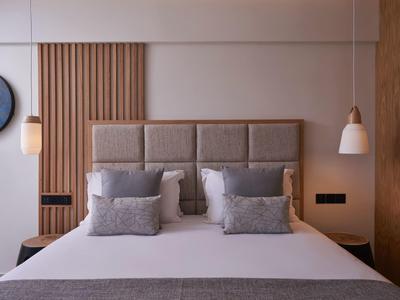 Modern hotel room with padded headboard, multiple pillows, and soft lighting.