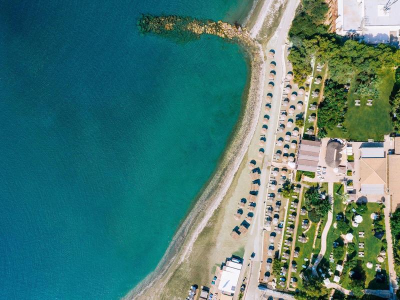Aerial view of a hotel with beach, sun umbrellas, and adjacent sea.