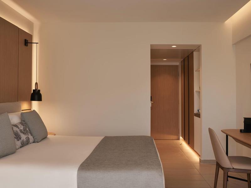 Modern hotel room with double bed, desk, and minimalist decoration.