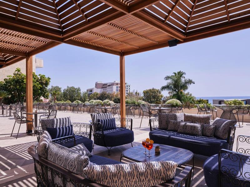 Sunny terrace with cushioned furniture and sea view at a hotel.