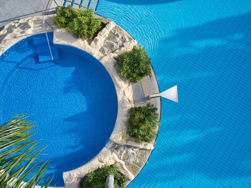 Round pool with blue water and stone wall, surrounded by plants and sun umbrella.