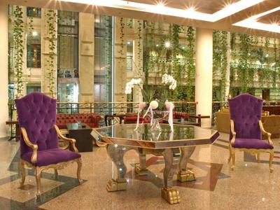 Área de vestíbulo lujosa con dos sillones morados y una mesa oval de cristal.