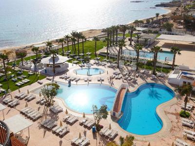 Vista de la piscina del hotel con tobogán, tumbonas y palmeras cerca de la playa.