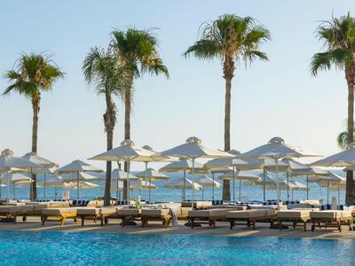 Área de piscina con tumbonas y sombrillas frente a palmeras y vista al mar