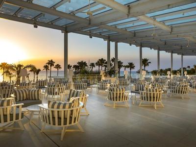 Zona de asientos abierta con sillas y mesas bajo una pérgola al atardecer junto al mar