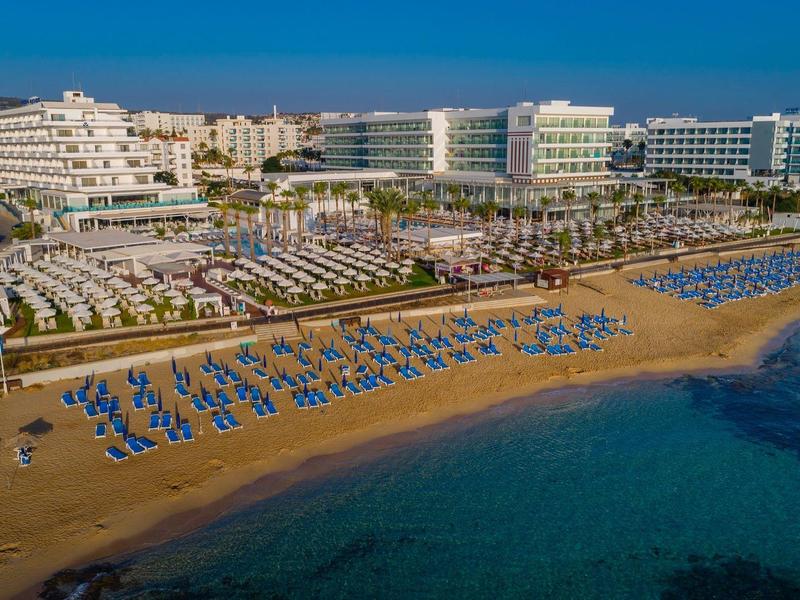 Strand mit blauen Liegestühlen, Sand, klarem Wasser und mehreren großen Hotels im Hintergrund.