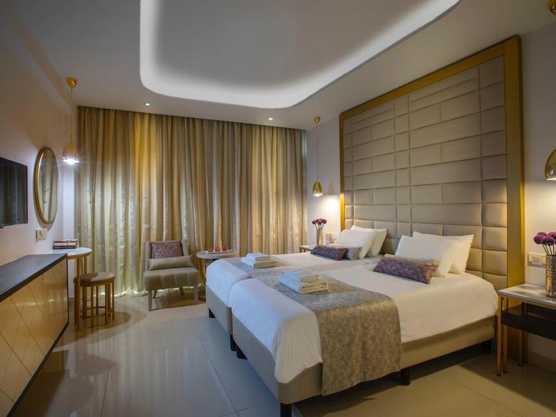 Modernes Hotelzimmer mit zwei Einzelbetten, beigen Vorhängen und indirekter Deckenbeleuchtung.