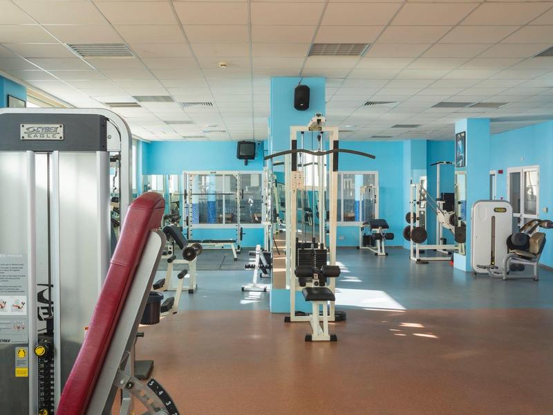 Heller, großer Fitnessraum mit blauen Wänden, verschiedenen Trainingsgeräten und Spiegeln.