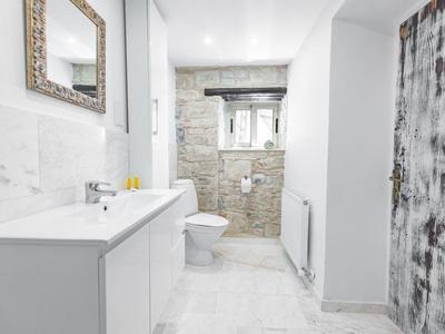 Helles Badezimmer mit weißem Waschbecken, Toilette und grauer Akzentwand aus Stein.