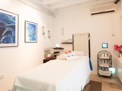 Heller Behandlungsraum mit Massageliege, weißen Wänden, Bildern und Klimaanlage.