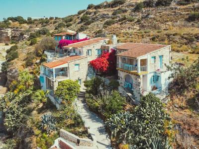 Dos casas de vacaciones mediterráneas rodeadas de colinas y vegetación.