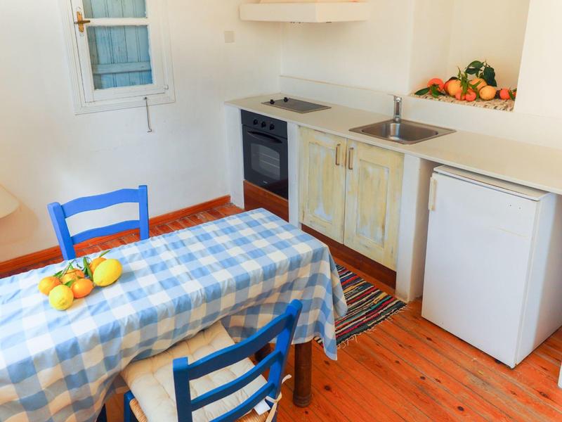 Kleine Küche mit blau kariertem Tischtuch, blauen Stühlen und Obst auf dem Tisch.