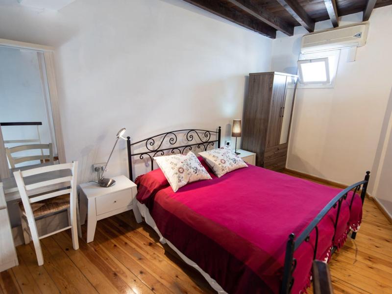 Gemütliches Schlafzimmer mit rustikalem Holzboden, rotem Bett und weißem Mobiliar unter sichtbaren Holzbalken.