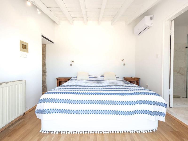 Helles Schlafzimmer mit Doppelbett, gestreifter Bettdecke und angrenzendem Bad mit Glasdusche.