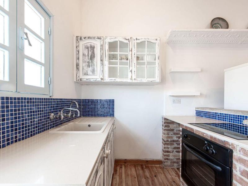 Kleine Küche mit weißen Schränken, blauen Fliesen und Backofen in einem hellen Raum.