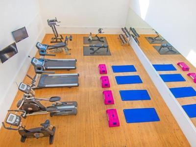 Palestra luminosa con tapis roulant, attrezzature, tappetini yoga blu e step rosa.