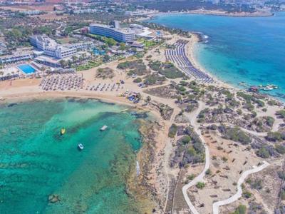 Veduta aerea di una spiaggia con acqua turchese e hotel sullo sfondo.