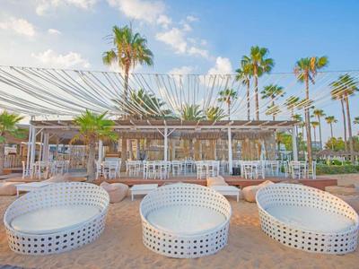 Bar sulla spiaggia con sedie a cesto bianche moderne e palme sotto un cielo sereno.