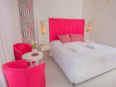 Schlafzimmer mit weißem Bett, pinkem Kopfteil, zwei pinken Sesseln und kleinem weißen Tisch.