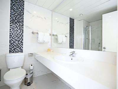 Helles, modernes Badezimmer mit weißer Einrichtung, großem Spiegel und Mosaikfliesen an der Wand.