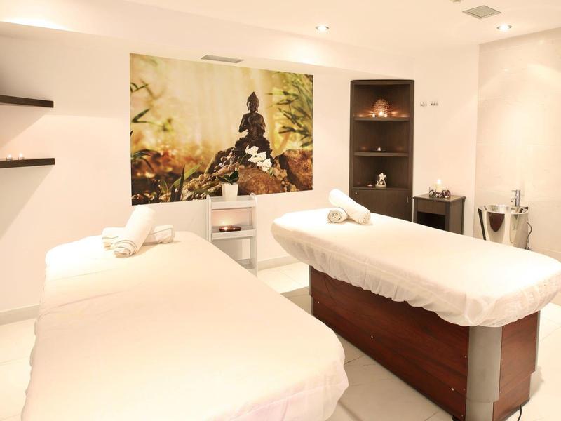 Heller Behandlungsraum mit zwei weißen Massageliegen, Wandbild und modernen Regalen.