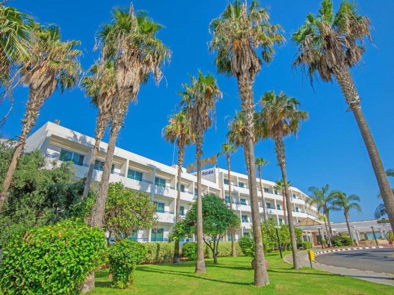 Mehrstöckiges weißes Gebäude mit Palmen und grünen Grasflächen unter klarem blauem Himmel.