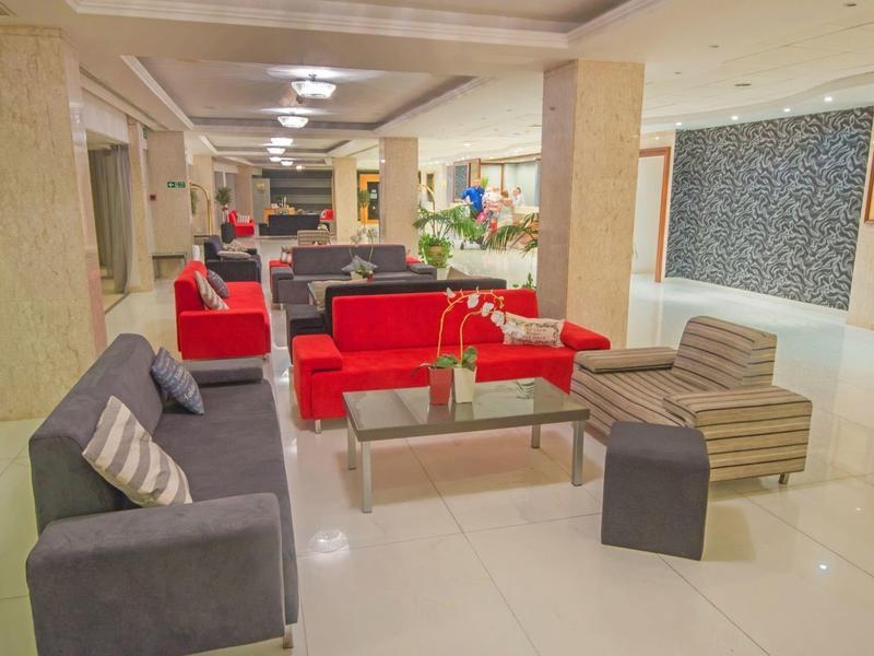 Großer heller Loungebereich mit roten und grauen Sofas, Glas-Tischen und poliertem Boden.