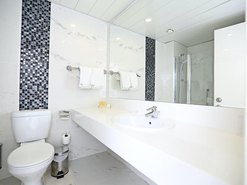 Helles, modernes Badezimmer mit weißer Einrichtung, großem Spiegel und Mosaikfliesen an der Wand.