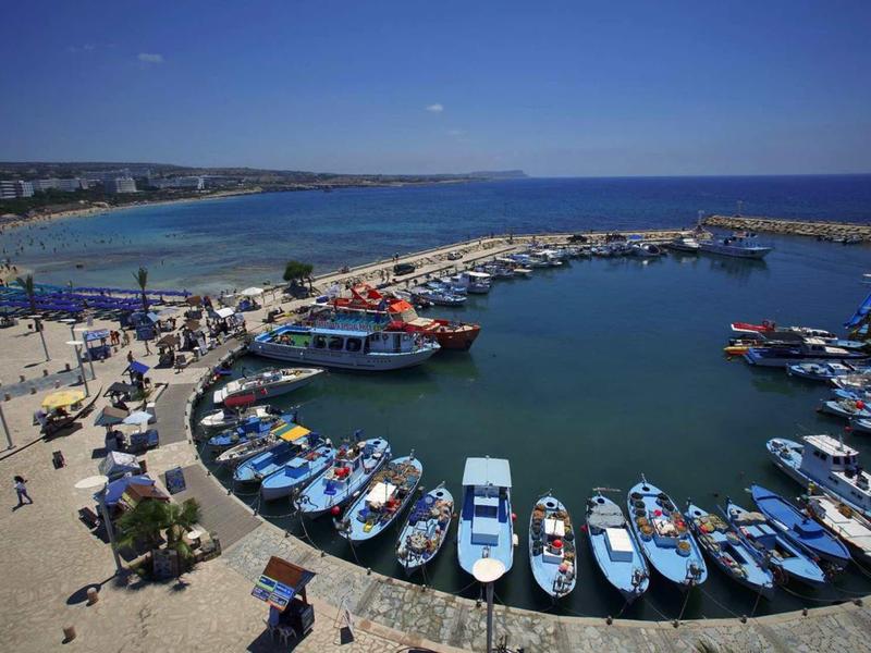 Kleiner Hafen mit vielen Booten und Menschen an einem sonnigen Tag am Meer.