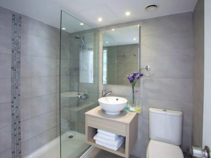 Modernes Badezimmer mit Glasdusche, weißem Waschbecken, grauen Fliesen und Toilettenanlage.