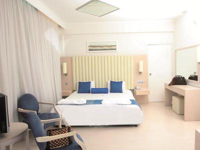 Hell eingerichtetes Hotelzimmer mit Doppelbett, zwei blauen Stühlen und Nachttischen.