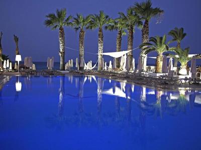 Ein großer, beleuchteter Pool umgeben von Palmen und Liegestühlen bei Nacht.