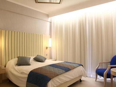 Modernes Hotelzimmer mit Doppelbett, blau-grauen Kissen und Vorhängen sowie einer Sitzgelegenheit.
