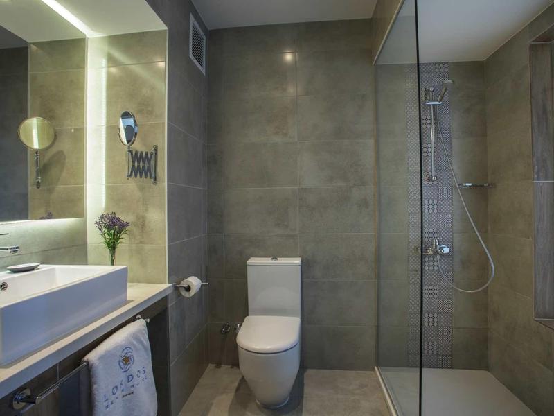 Modernes Badezimmer mit grauen Fliesen, weißem WC, Waschbecken und Glas-Dusche.