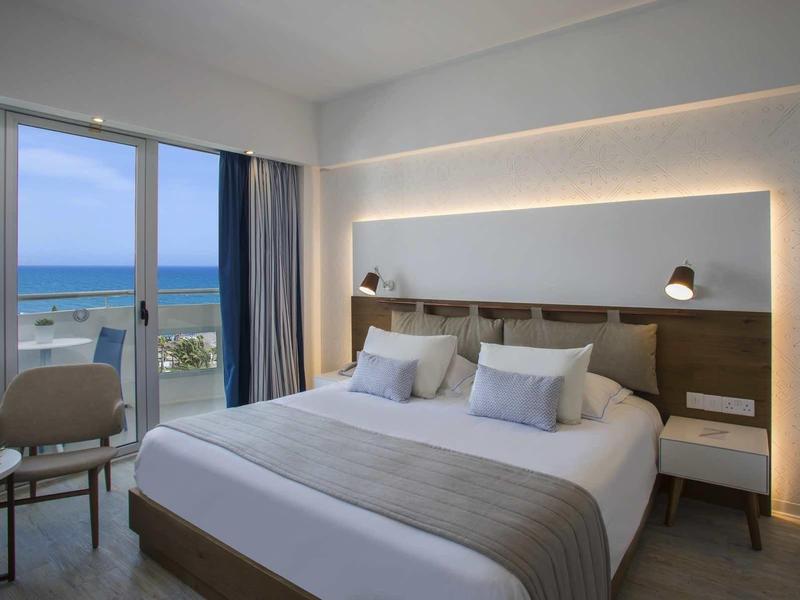 Modernes Schlafzimmer mit Doppelbett, sanfter Beleuchtung und Meerblick durch große Fenster.