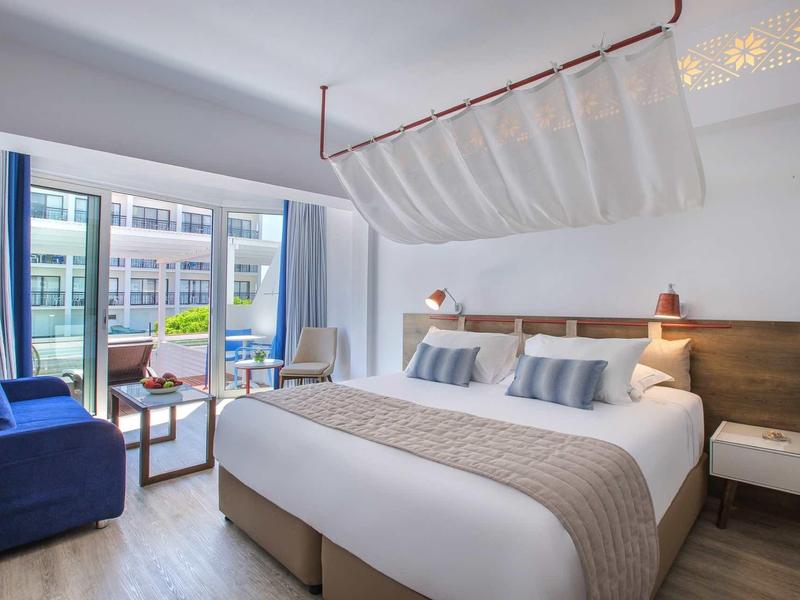 Modernes Hotelzimmer mit Doppelbett, blauen Vorhängen, Sofa und Balkon mit Blick nach draußen.