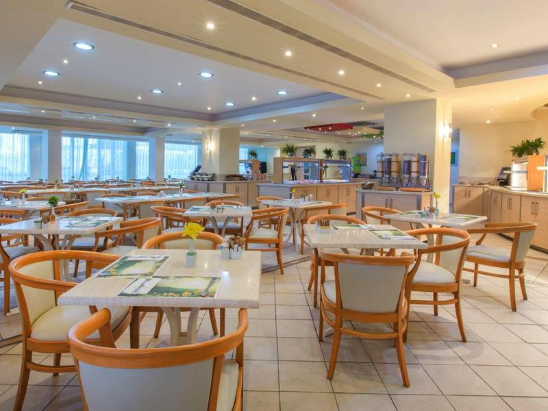 Helles Restaurant mit Holztischen, Stühlen und großem Buffetbereich am rechten Rand.