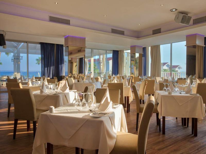 Elegantes Restaurant mit eingedeckten Tischen, beigen Stühlen und großen Fenstern mit Meeresblick.