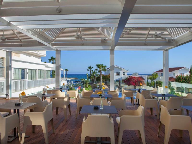 Offener Restaurantbereich mit Stühlen und Tischen, Blick auf Meer und Gebäude im Hintergrund.