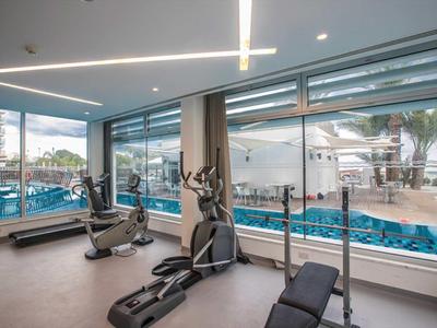 Posilovna s kardio vybavením a velkými okny s výhledem na bazén.