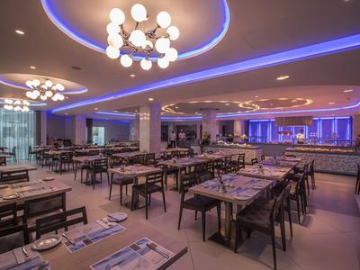 Moderní osvětlená restaurace se stoly a židlemi v jasném interiéru.